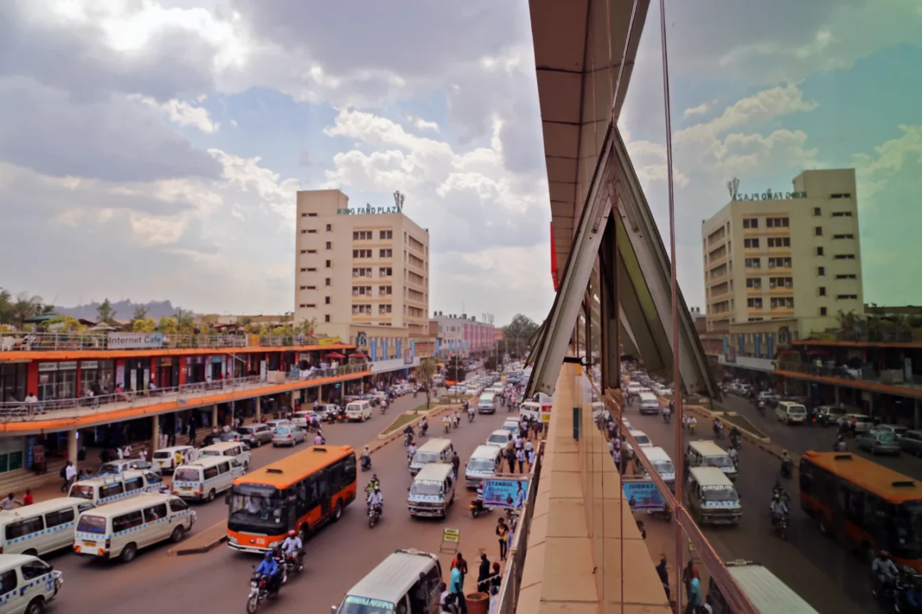 Street activity and buildings along Kampala Road, with a reflected view in the adjacent facade